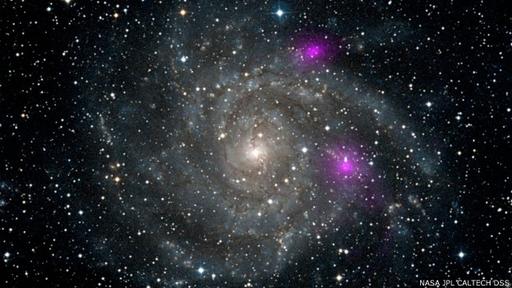 En 2012, Nustar registró rayos X de alta energía (en magenta) emitidos por dos agujeros negros cerca de la galaxia en espiral IC 342.