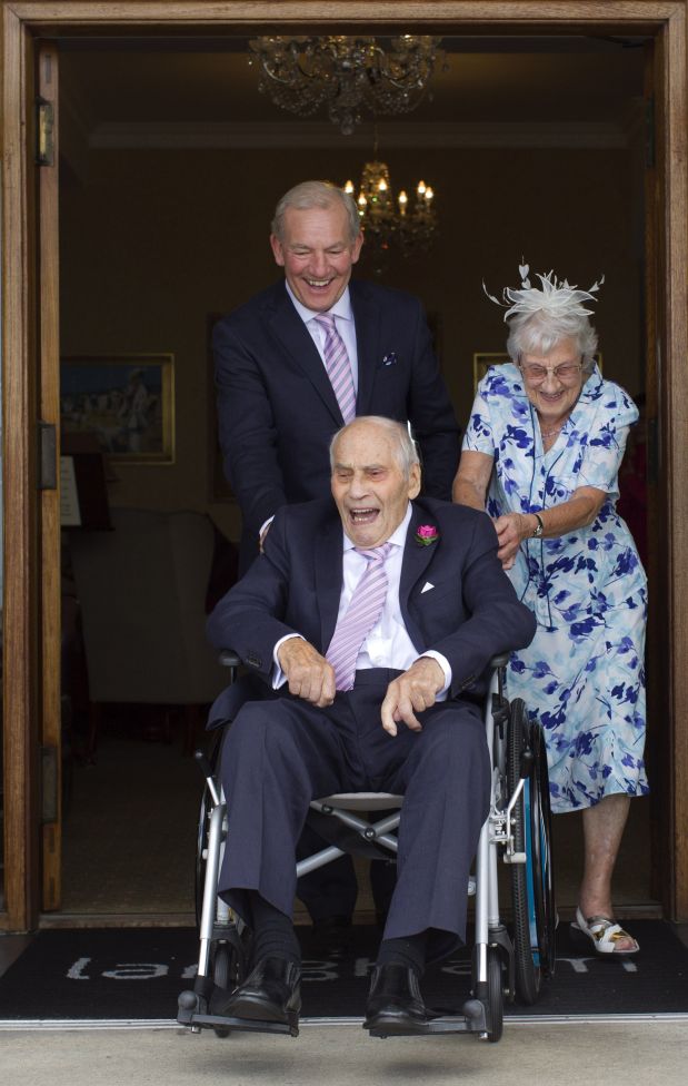 George Kirby, aged 103 (C), is pushed outside in his wheelchair by wife Doreen Luckie (R), 91, and George's son Neil Kirby (back) after their wedding ceremony at the Langham Hotel in Eastbourne, southern England, on June 13, 2015. Doreen and George are thought to be the oldest couple in the world to get married. AFP PHOTO / JUSTIN TALLIS