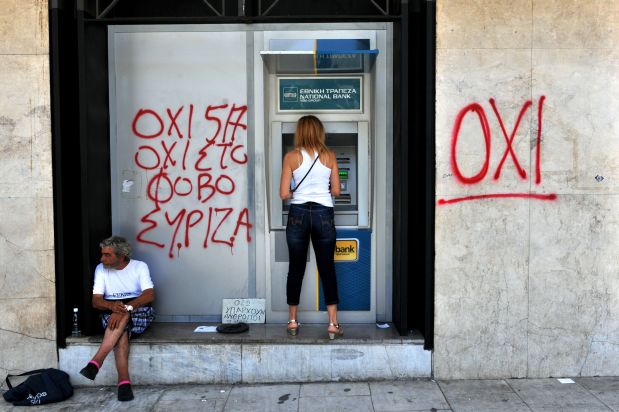 A woman withdraws money from an ATM machine next to a beggar and a graffiti reading
