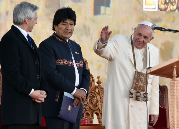Pope Francis (R) waves next to Bolivian President Evo Morales (C) and Vice-President Alvaro Garcia Linera during a ceremony in El Alto, upon landing in the country on July 8, 2015. Pope Francis, the first Latin American pontiff, arrived in Bolivia on the second leg of a three-nation tour of the continent's poorest countries, where he has been acclaimed by huge crowds.  AFP PHOTO / CRIS BOURONCLE