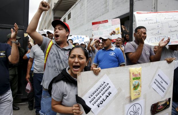 Empresas Polar workers hold placards and shout at the gate of a facility used by the company as a distribution center, during the occupation of its installations by government representatives in Caracas July 30, 2015. The placard reads: 