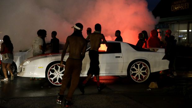 A person accelerates a car, causing the back tires to smoke, along West Florissant Avenue, Sunday, Aug. 9, 2015, in Ferguson, Mo. Sunday marks one year since Michael Brown was shot and killed by Ferguson police officer Darren Wilson. (AP Photo/Jeff Roberson)