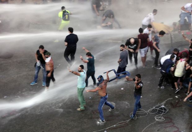 Lebanese activists shout anti-government slogans and throw objects as they are sprayed by riot police using water cannons during a protest against the ongoing trash crisis, in downtown Beirut, Lebanon, Sunday, Aug. 23, 2015. Lebanese riot police are spraying thousands of protesters with water cannons in downtown Beirut, the second day of mass demonstrations against an ongoing trash crisis becoming violence. (AP Photo/Bilal Hussein)