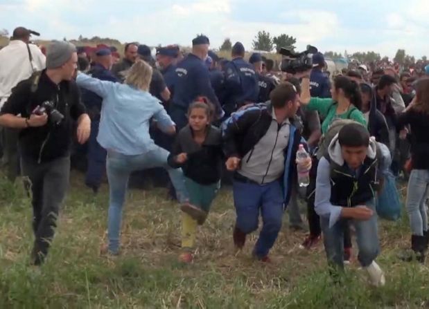 In this image taken from TV a Hungarian camerawoman, center left in blue, kicks out at a young migrant who had just crossed the border from Serbia  near Roszke Hungary Tuesday Sept. 8, 2015. The camerawoman has been fired after she was caught on video kicking and tripping migrants entering Hungary across the border with Serbia. The N1TV Internet channel said their employee, widely identified in Hungarian media as Petra Laszlo, has been dismissed because she 