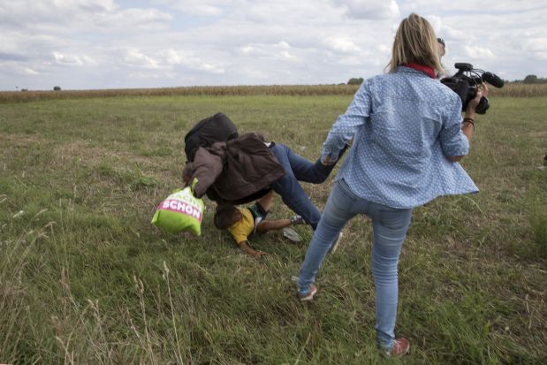 A migrant carrying a child falls after tripping on a TV camerawoman (R) while trying to escape from a collection point in Roszke village, Hungary, September 8, 2015. REUTERS/Marko Djurica