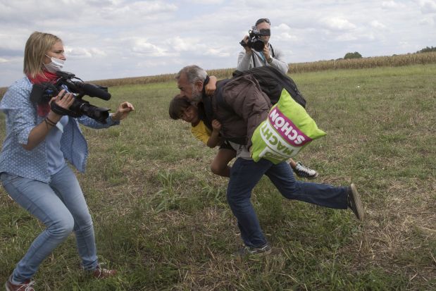 REFILE - ADDITIONAL INFORMATIONA migrant runs with a child before tripping on TV camerawoman Petra Laszlo (L) and falling as he tries to escape from a collection point in Roszke village, Hungary, September 8, 2015. Laszlo, a camerawoman for a private television channel in Hungary, was fired late on Tuesday after videos of her kicking and tripping up migrants fleeing police, including a man carrying a child, spread in the media and on the internet.  REUTERS/Marko Djurica