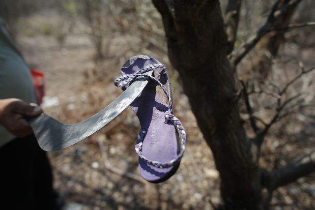In this April 22, 2015 photo, a man inspects a sandal during a search for clandestine graves in the dry brush on the outskirts of Iguala, Mexico. Authorities are of little help, say residents who have seen local police escorting gangsters through town and consider them to be a uniformed extension of Guerreros Unidos. That relationship was reinforced by the government investigation into the case of the 43 students, which concluded that Iguala and Cocula police had turned them over to members of Guerreros Unidos, who then killed them and disposed of the incinerated remains in Cocula.  (AP Photo/Dario Lopez-Mills)