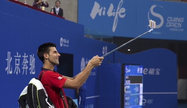 Novak Djokovic of Serbia uses a mobile phone to take a selfie with spectators after winning the first round men's singles match against Simone Bolelli of Italy in the China Open tennis tournament at the National Tennis Stadium in Beijing, Tuesday, Oct. 6, 2015. (AP Photo/Andy Wong)