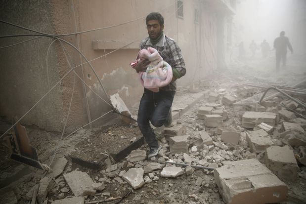 A Syrian man carries a baby wrapped in a blanket following air strikes on the town of Douma in the eastern Ghouta region, a rebel stronghold east of the capital Damascus, on December 13, 2015. At least 28 civilians were killed in heavy bombardment of the besieged Syrian rebel stronghold, including near a school, according to the Syrian Observatory for Human Rights.  AFP PHOTO / SAMEER AL-DOUMY