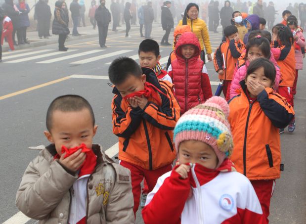 This photo taken on December 23, 2015 shows pupils from an elementary school covering their mouths and noses as they leave the schoolyard after the classes were suspended because of a 