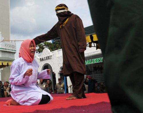 A young Acehnese woman (L) is caned in public, a punishment under the Islamic sharia law, under the offence of 