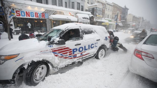 People pitch in to get a DC Metro police car moving again on 18th Street NW, Saturday, Jan. 23, 2016 in Washington. A blizzard with hurricane-force winds brought much of the East Coast to a standstill Saturday, dumping as much as 3 feet of snow, stranding tens of thousands of travelers and shutting down the nation's capital and its largest city. (AP Photo/Alex Brandon)