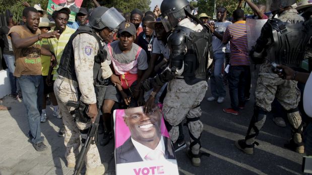 A protester pushes a suitcase covered with a poster of presidential candidate Jovenel Moise between two National Police officers near the National Palace during a demonstration called up by opposition groups in Port-au-Prince, Haiti, February 6, 2016. REUTERS/Andres Martinez Casares