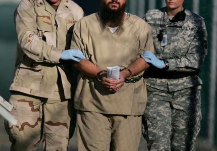** FILE ** In this Dec. 6, 2006 file photo, reviewed by the U.S. Military, a shackled detainee clutching paperwork of some kind is escorted by two gloved U.S. Military personnel to an Annual Review Board Hearing in Camp Delta detention facility on Guantanamo Bay U.S. Naval Base in Cuba. A Saudi government spokesman said Wednesday, Feb. 4, 2009 that 11 of the Saudis on its recently issued most wanted list are former Guantanamo detainees. (AP Photo/Brennan Linsley,File)