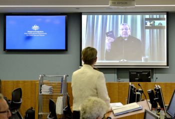 Senior Counsel Assisting Gail Furness stands in front of a screen displaying Australian Cardinal George Pell as he holds a bible while appearing via video link from a hotel in Rome, Italy to testify at the Australia's Royal Commission into Institutional Response to Child Sexual Abuse in Sydney, Australia, February 29, 2016. Australian Cardinal George Pell said on Sunday the Catholic Church had made 
