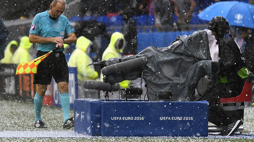 Assistant referee Slovakian Roman Slysko (L) leaves the pitch during a hailstorm during the Euro 2016 group C football match between Ukraine and Northern Ireland at the Parc Olympique Lyonnais stadium in D?cines-Charpieu near Lyon on June 16, 2016. / AFP / PHILIPPE DESMAZES
