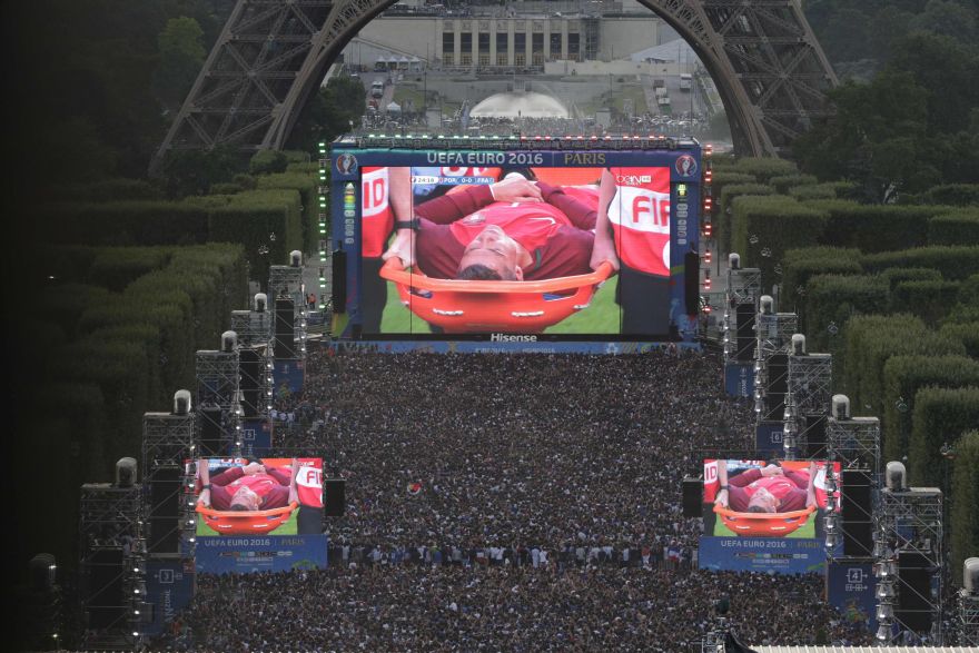 People watch on a giant screen the Euro 2016 football tournament final match between Portugal and France, while Portuguese forward Cristiano Ronaldo is evacuated on a stretcher after being injured, on July 10, 2016 at the fan zone of the Champs de Mars near the Eiffel tower in Paris. / AFP / GEOFFROY VAN DER HASSELT
