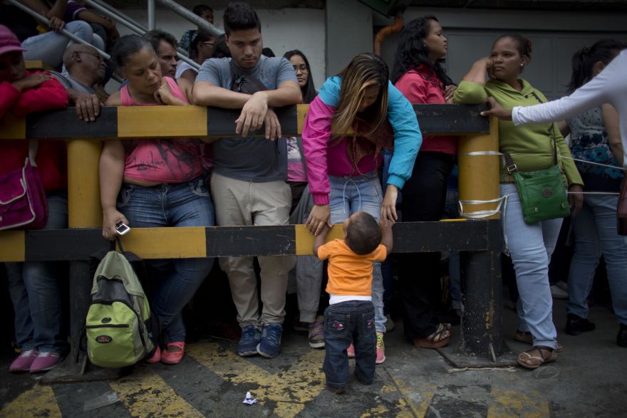 In this Tuesday, May 3, 2016, photo, sixteen-year-old Madeley Vasquez stands with her one-year-old son Joangel outside a supermarket as she waits to buy food in Caracas, Venezuela. Joangel was still experimenting with tentative steps when it came time for his mother to buy her two bags of rice and two packets of toilet paper. (AP Photo/Ariana Cubillos)