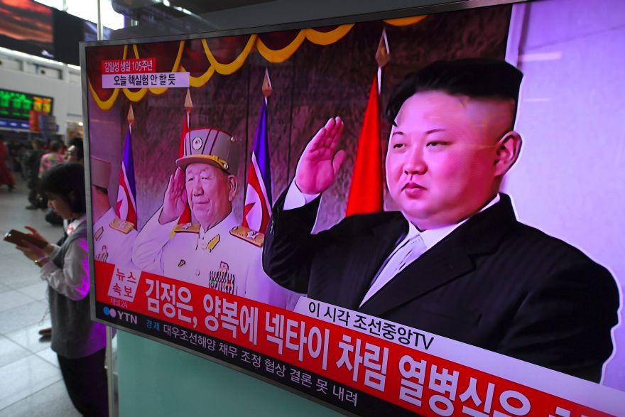 People walk past a television screen broadcasting live footage of a parade to mark the 105th anniversary of the birth of North Korea's founder Kim Il-Sung and showing North Korean leader Kim Jong-Un (R), at a railway station in Seoul on April 15, 2017. North Korean leader Kim Jong-Un on April 15 saluted as ranks of goose-stepping soldiers followed by tanks and other military hardware paraded in Pyongyang for a show of strength with tensions mounting over his nuclear ambitions. / AFP / JUNG Yeon-Je